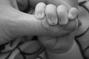 A baby's fingers wrapped around an adult's thumb