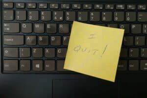 A yellow sticky note with the writing "I Quit!" sits atop a black keyboard.