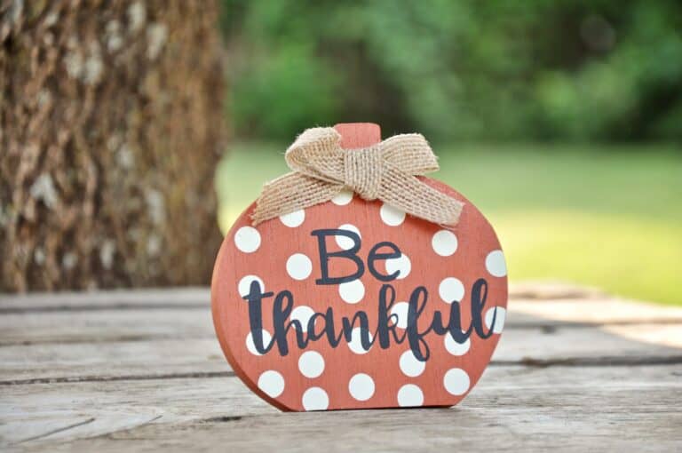 A painted wooden pumpkin with polka dots has the words be thankful in black, script writing.