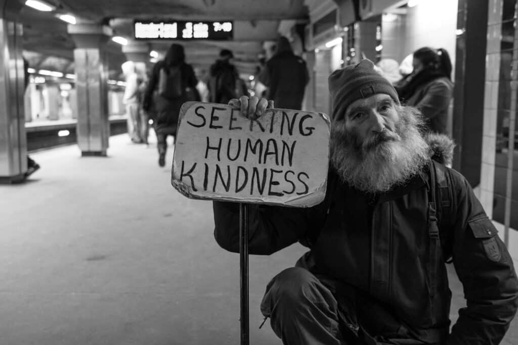 A man sits in a subway station holding a sign that says "seeking human kindness"