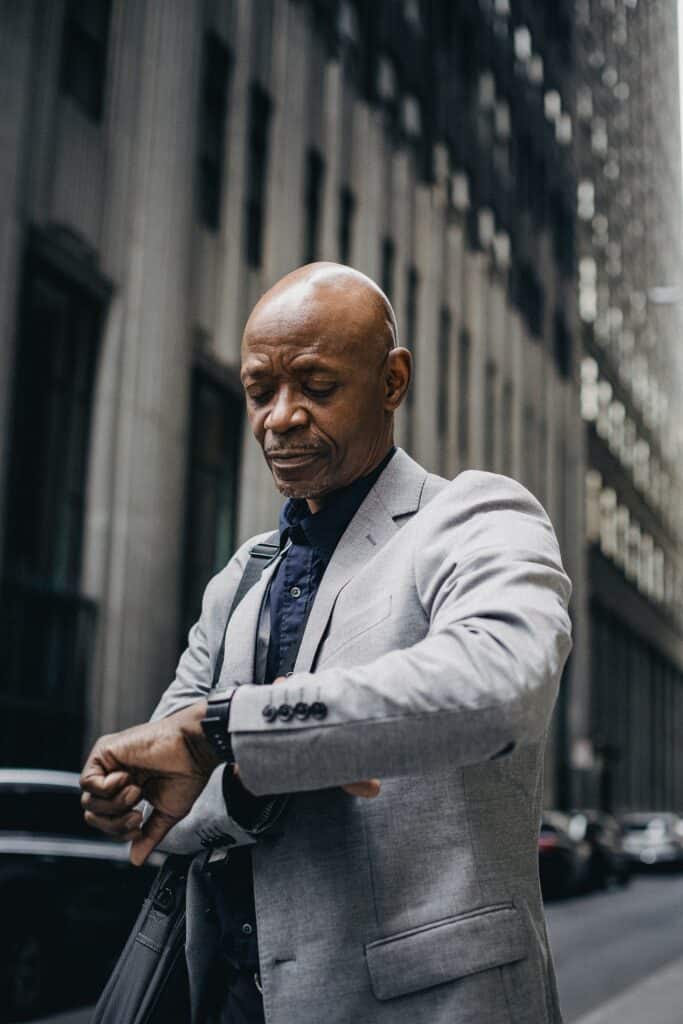 A mature man stands on the street in his business suit looking at his watch