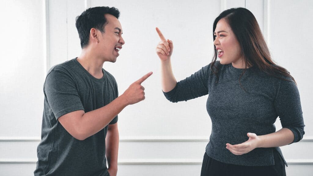 A man and woman look angrily and point fingers at one another.