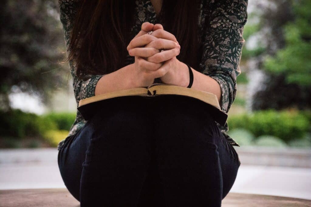 The hands of a woman folded on top of a Bible.