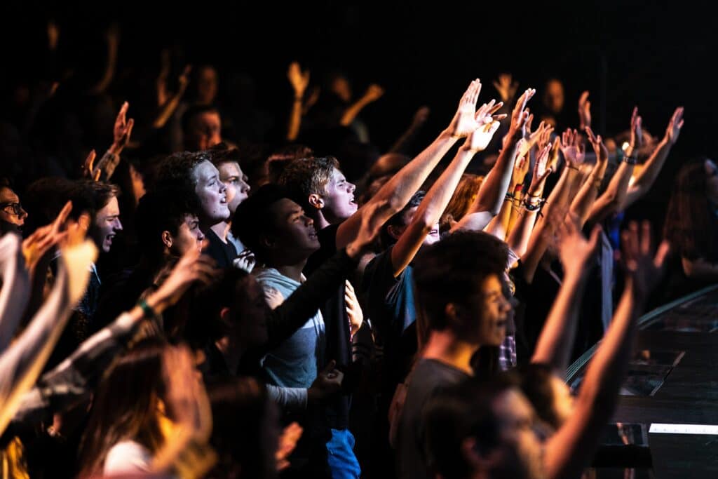 A group of people stand in a crowd with their hands lifted.