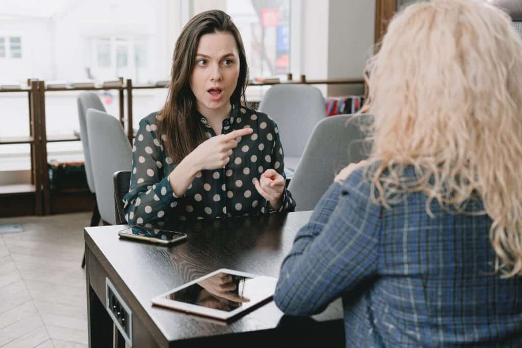 A woman is facing another woman at a table and pointing her finger.