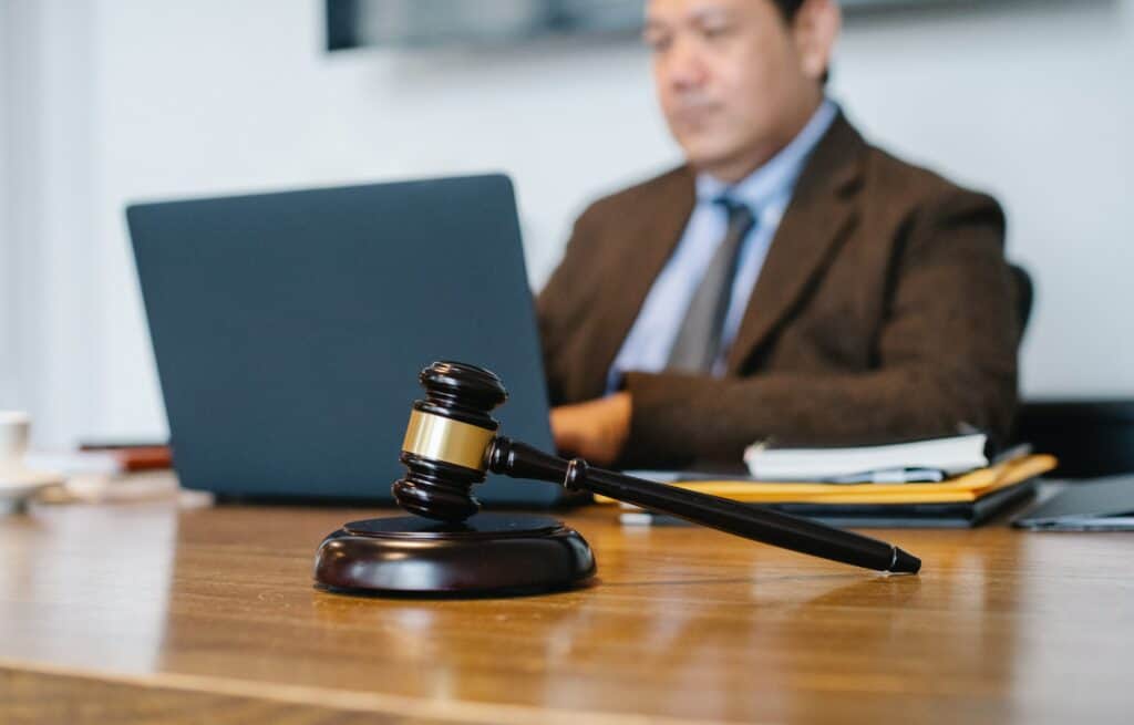 An Asian man sits at a laptop with a gavel and block