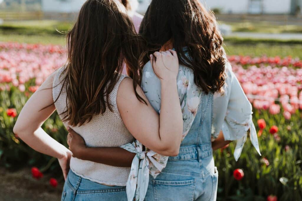 Two women stand with their arms around each other's backs, facing away from the camera.