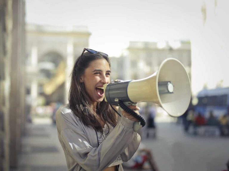 A woman smiles holding a bullhorn while she talks into it.