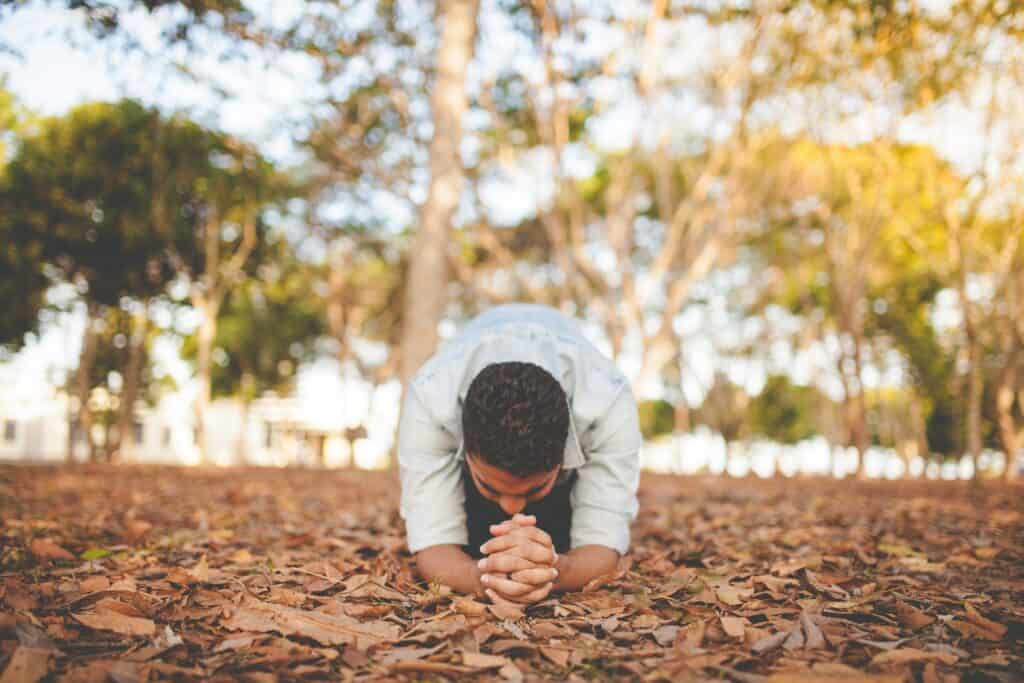 A man is in the middle of the woods kneeled down praying