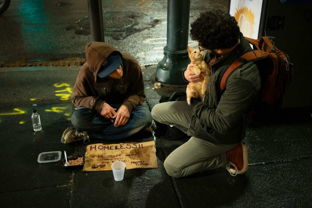 A man sits with a homeless man