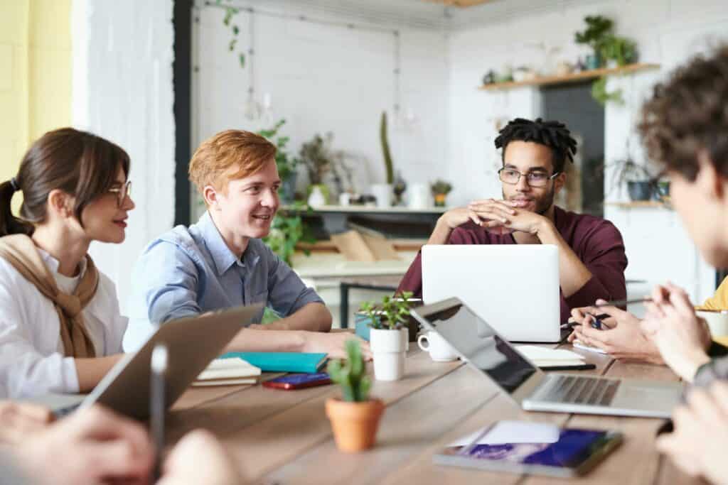 A group of employees sit around a table with their laptops