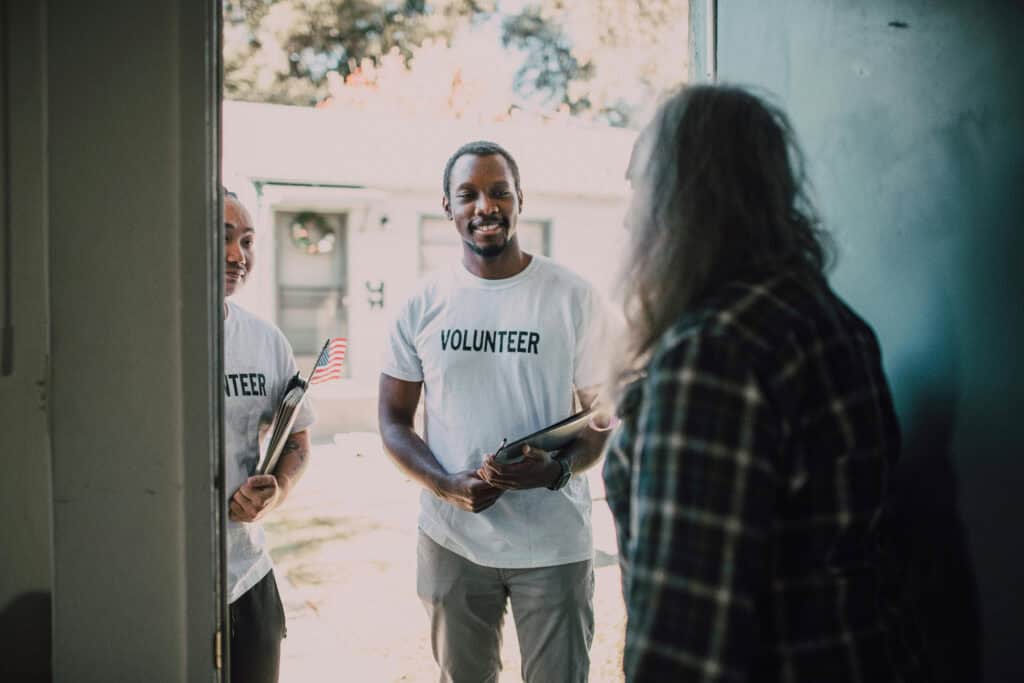 Two volunteers stand at a man's door.