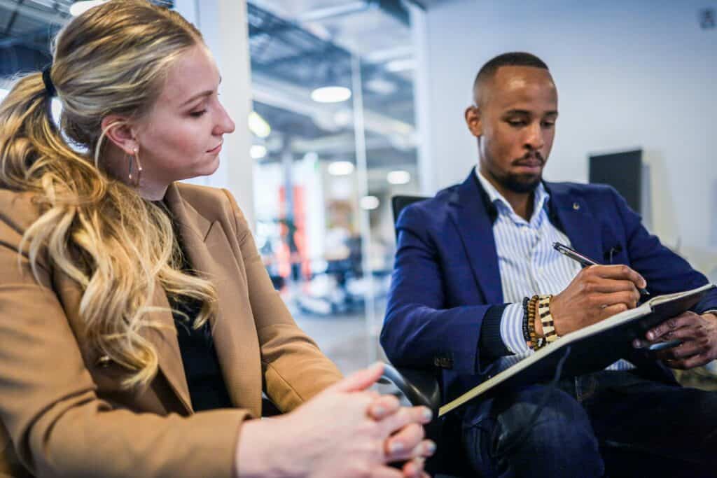 A black man and a white woman sit together looking at a notebook.