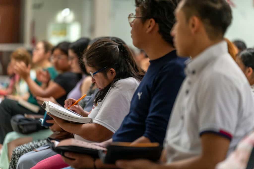 A group of people with books and pens are sitting down